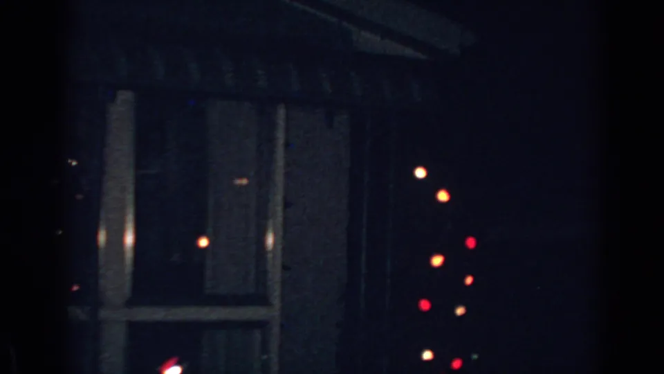 Nighttime 1962 Gary, Indiana frame with a dim residential wall, window, and soft red and orange Christmas lights.
