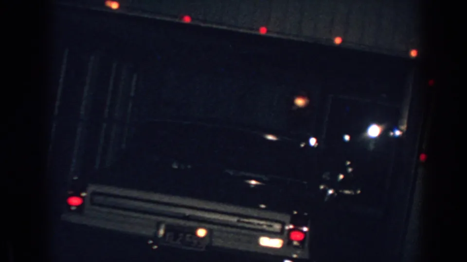 1962 Gary, Indiana home-movie frame showing a parked car before a dark garage door with small holiday lights nearby.