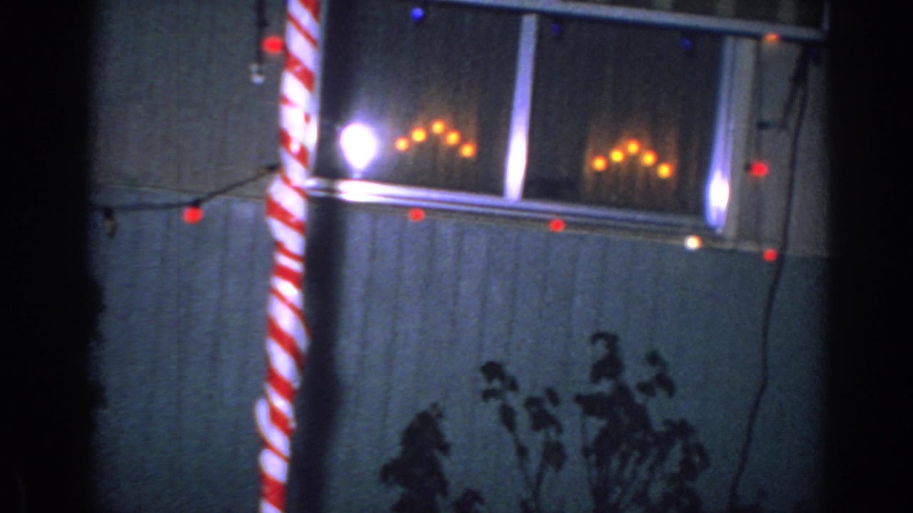 Window outlined with Christmas lights and a striped candy-cane decoration outside a house.