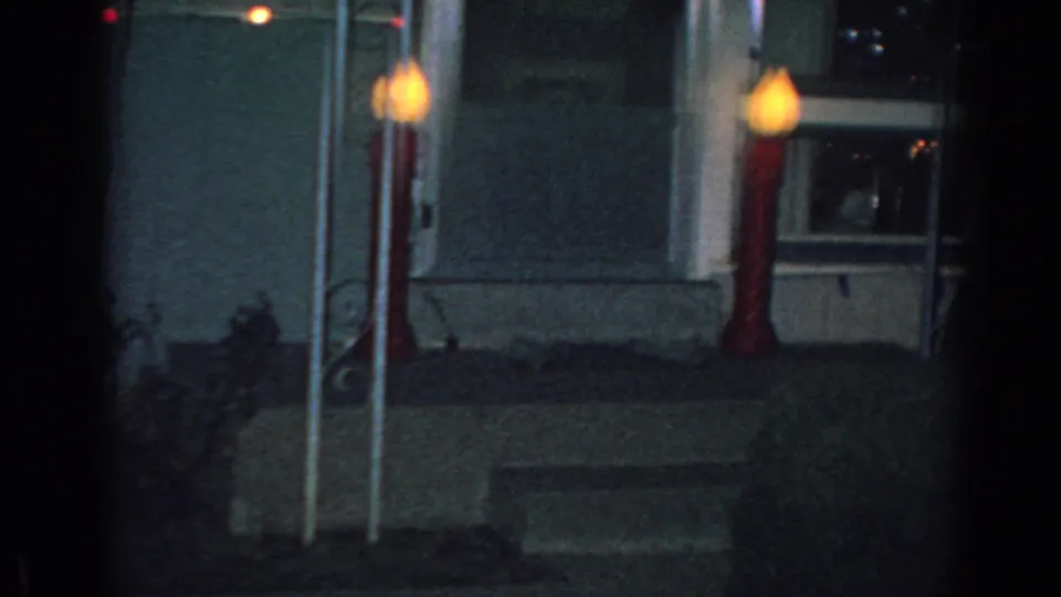 1962 Gary, Indiana frame showing a residential entry area at night with two tall red-and-white candy-cane decorations, a small lit window, house siding, and a dark walkway.