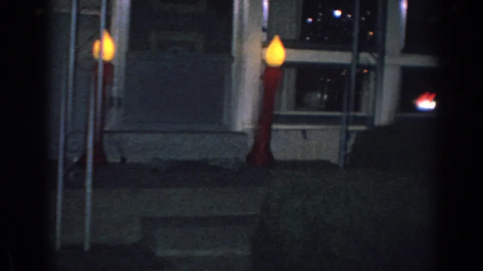 1962 Gary, Indiana home-movie frame showing a dark house exterior with two large illuminated candle decorations near the porch steps.