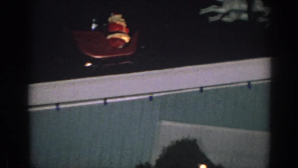 1962 Gary, Indiana home-movie frame with a Santa Claus figure on the roofline above the house and holiday lights nearby.