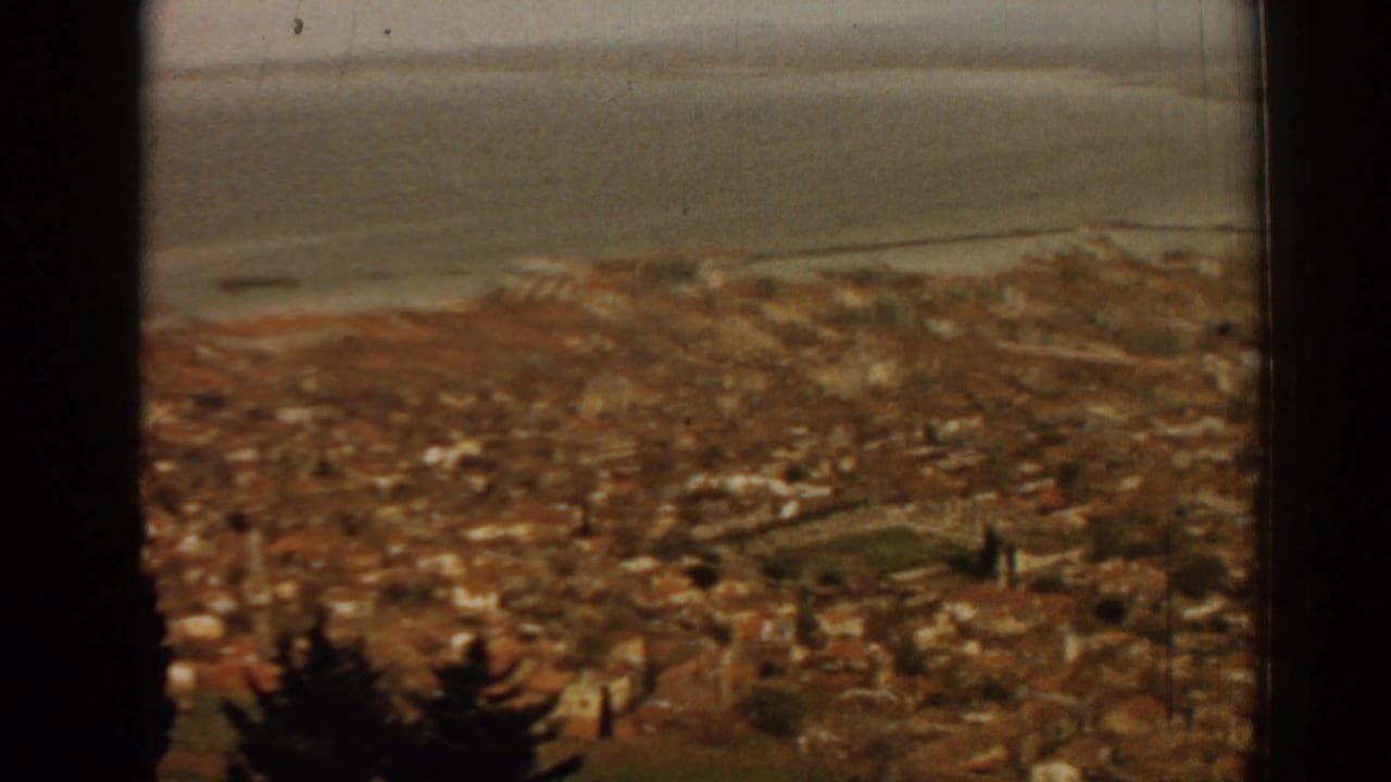 1962 8mm view from a high window over Izmir rooftops toward the bay, with dark window edges framing the scene.