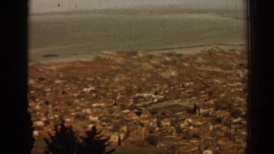 1962 8mm view from a high window over Izmir rooftops toward the bay, with dark window edges framing the scene.