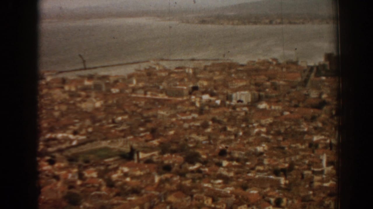 Elevated view over dense rooftops toward water and a hazy horizon.