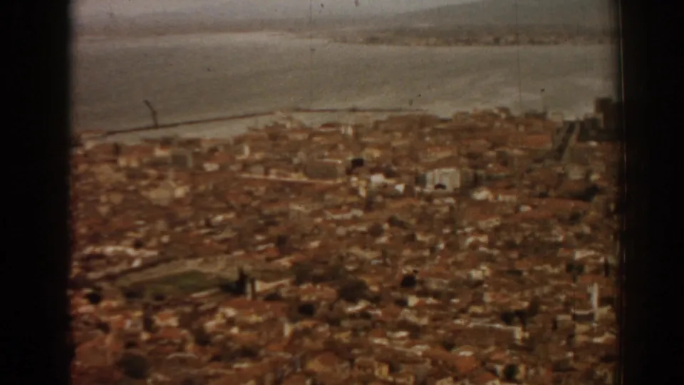 1962 8mm view over Izmir rooftops toward the bay, with soft focus and dark film-gate edges.