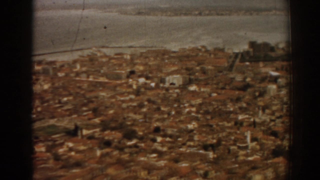 City rooftops spread below a waterfront, with a dark vertical film strip at left.