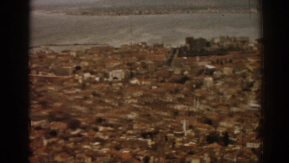 Izmir city panorama from 1962 8mm footage, with rooftops, bay, and a prominent hilltop structure in the distance.