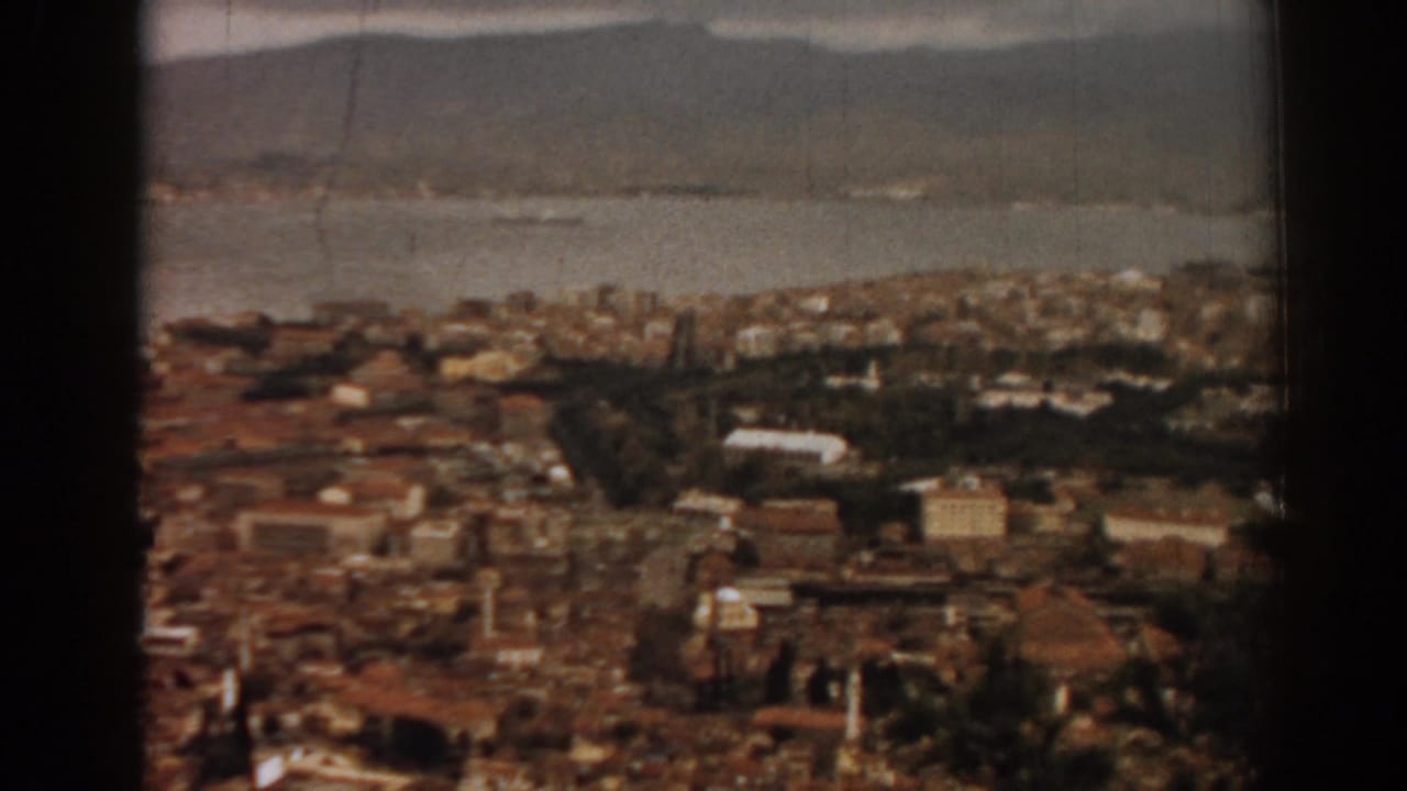 1962 8mm view over Izmir, Turkey, showing dense rooftops, bay water, and mountains in soft color.