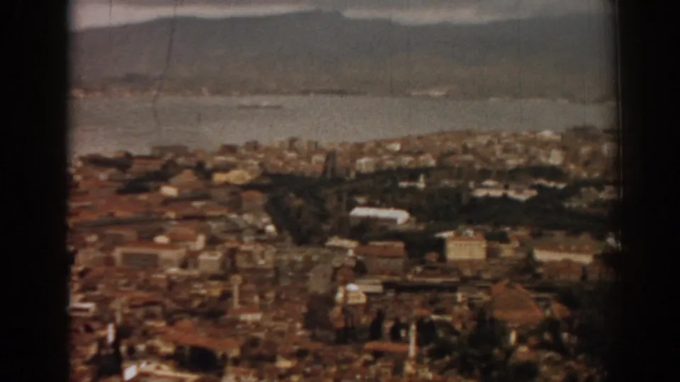 1962 8mm view over Izmir, Turkey, showing dense rooftops, bay water, and mountains in soft color.