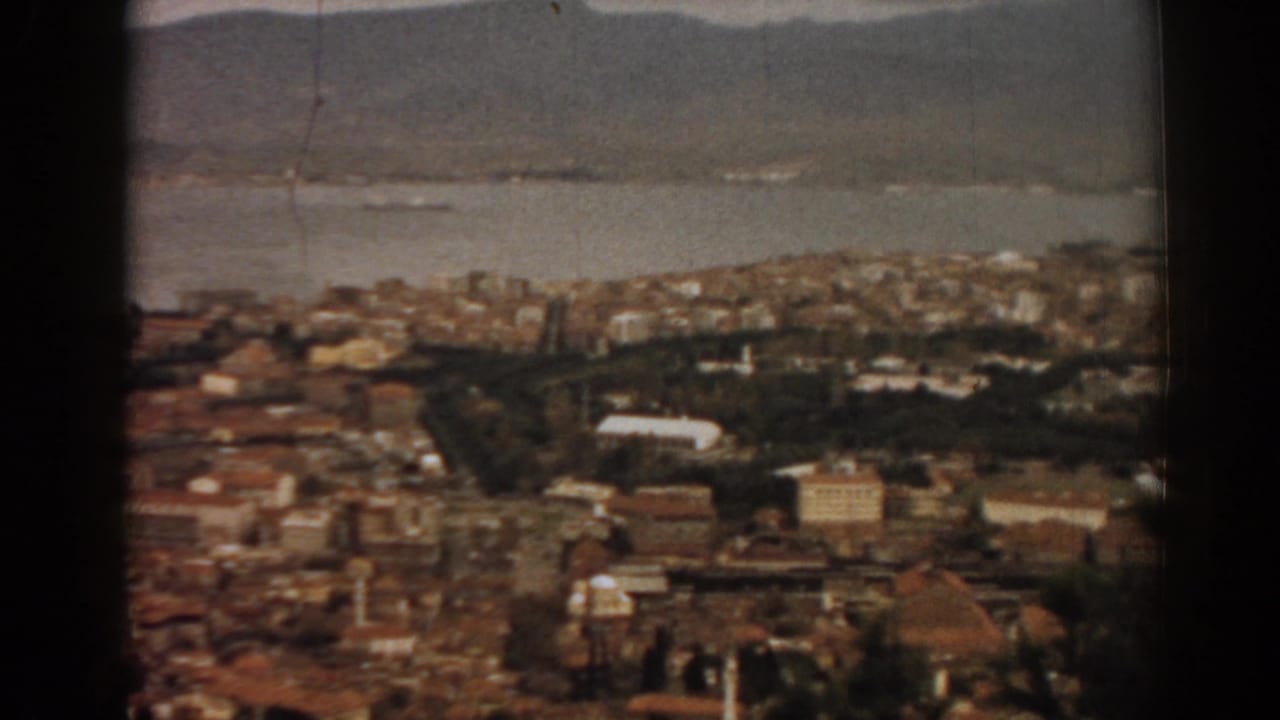 City rooftops and shoreline with bay water and mountains beyond.