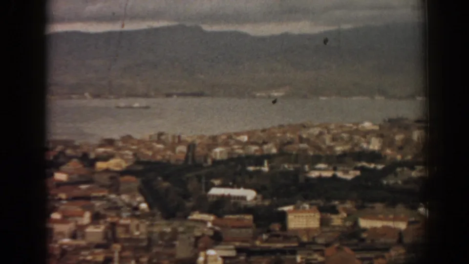 Soft 8mm frame of Izmir from above, showing city blocks, harbor water, several vessels, and mountains.