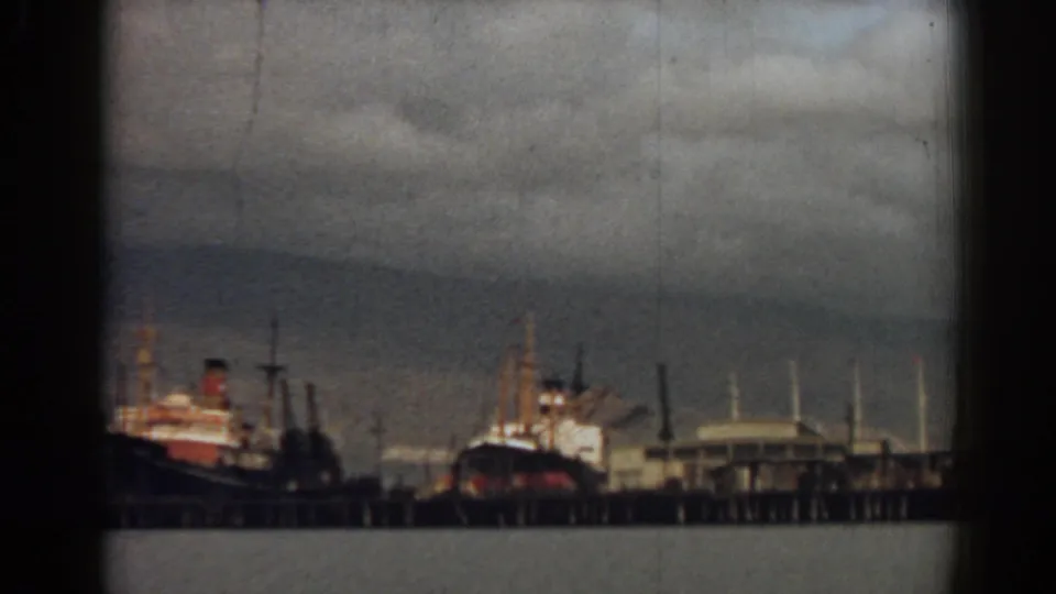 Izmir harbor scene from 1962 showing moored ships, pier pilings, and waterfront structures through soft 8mm film borders.