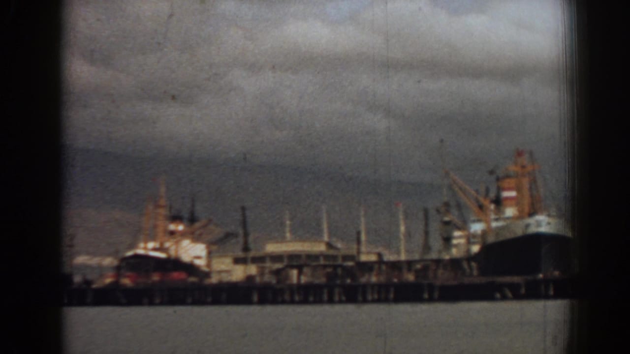1962 8mm view of ships moored at the Izmir waterfront, with cranes, pier structures, and harbor water visible.