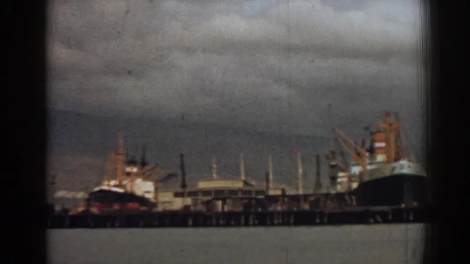 1962 8mm view of ships moored at the Izmir waterfront, with cranes, pier structures, and harbor water visible.