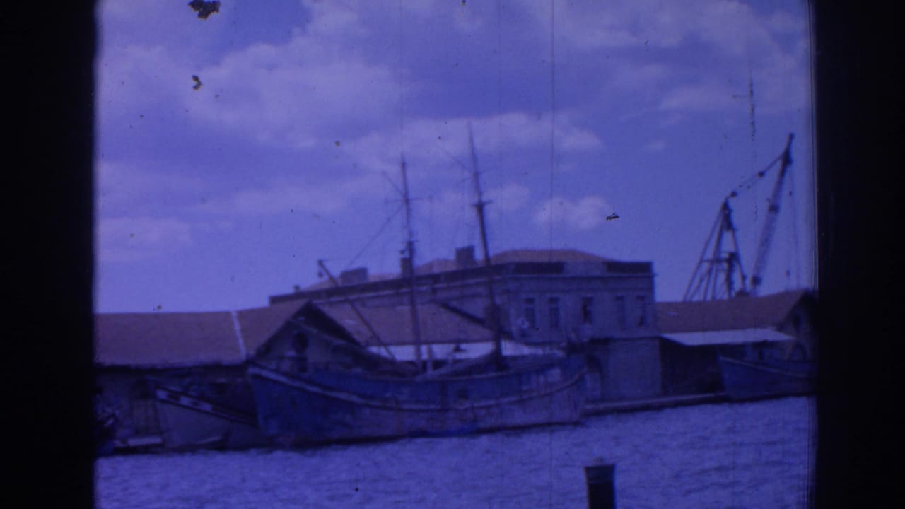 Waterfront boats and a large building with cranes or rigging behind the quay.