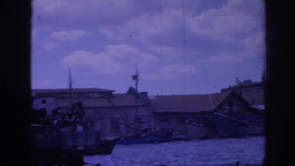 End of the harbor pan in Izmir, showing rigging, a small flag, quay buildings, water, and part of a moored vessel at frame edge.