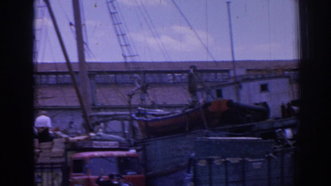 Harbor boats and stacked cargo seen through a dark window-like frame.