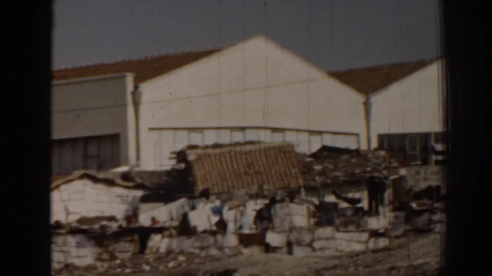 1962 Izmir frame showing informal housing and people at a distance beneath a large white gabled building.