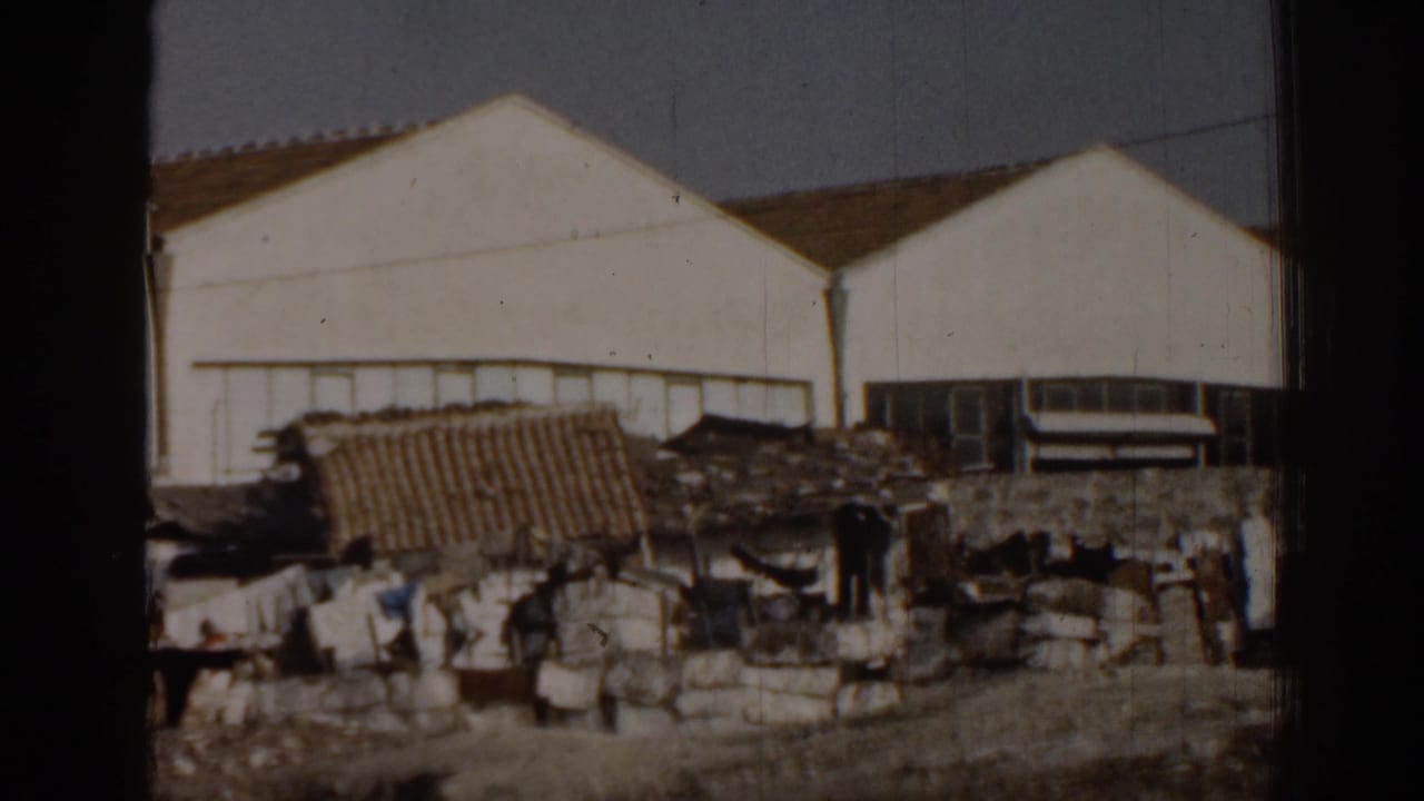 Industrial buildings, debris piles, a tiled roof, and dark figures near rough structures.