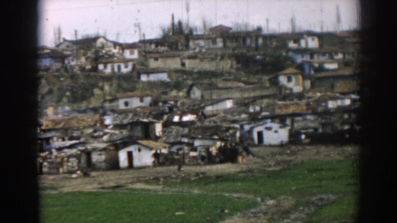 1962 Izmir hillside settlement with dense white-painted homes, rough roofs, and a green foreground strip.
