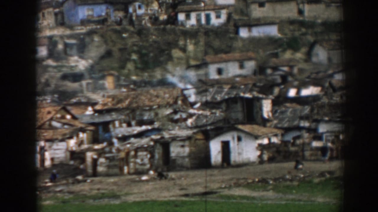 Distant hillside village with clustered small houses, rough roofs, open ground and tiny figures.