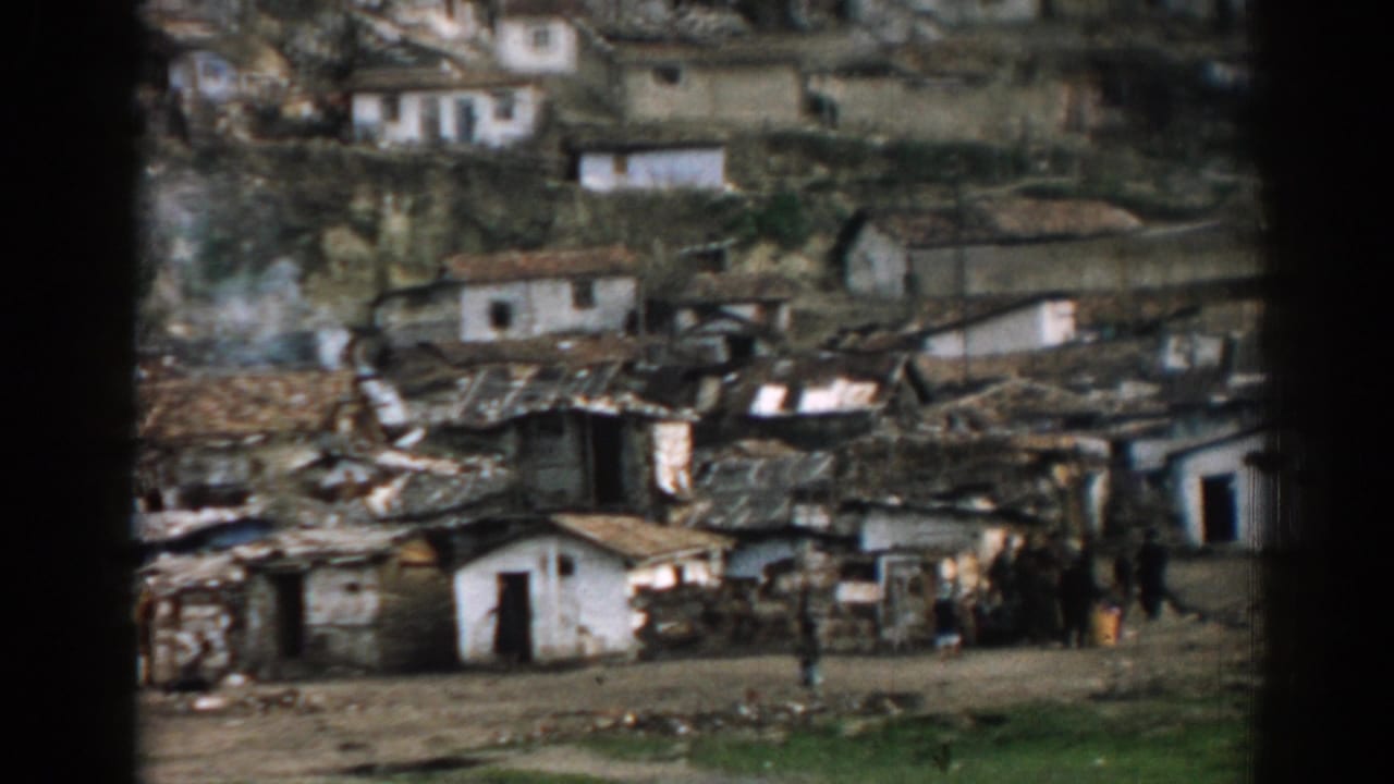 Hillside homes with burned roofs, debris, and people standing near damaged structures.