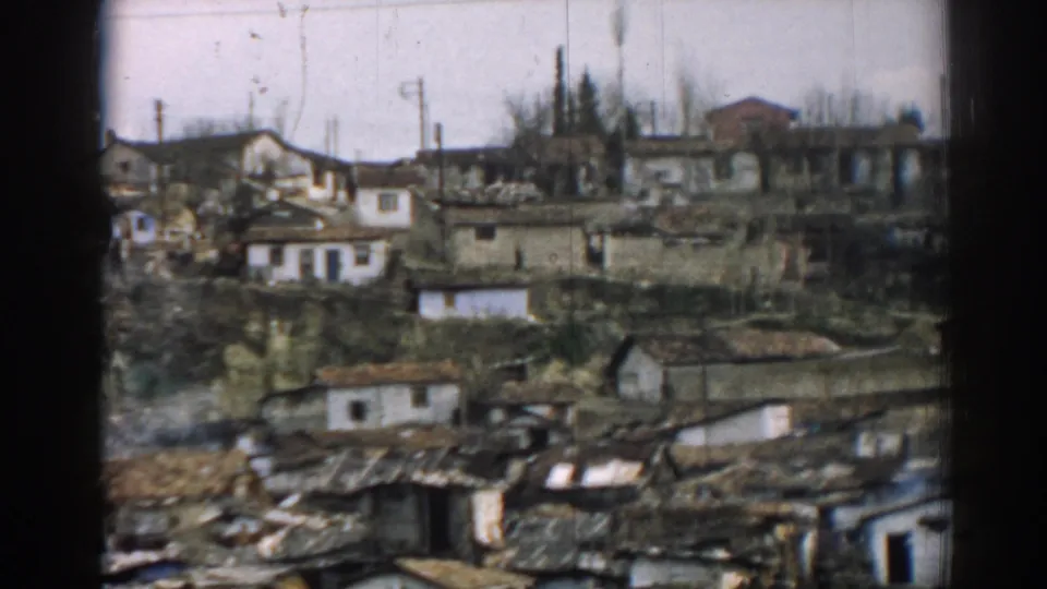 Izmir hillside homes with visible roof damage, bare trees, and scattered debris in soft 8mm color.