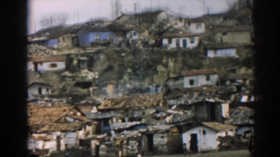 Wide 1962 Izmir view of fire-damaged hillside houses, collapsed roofing, rubble, and distant residents.