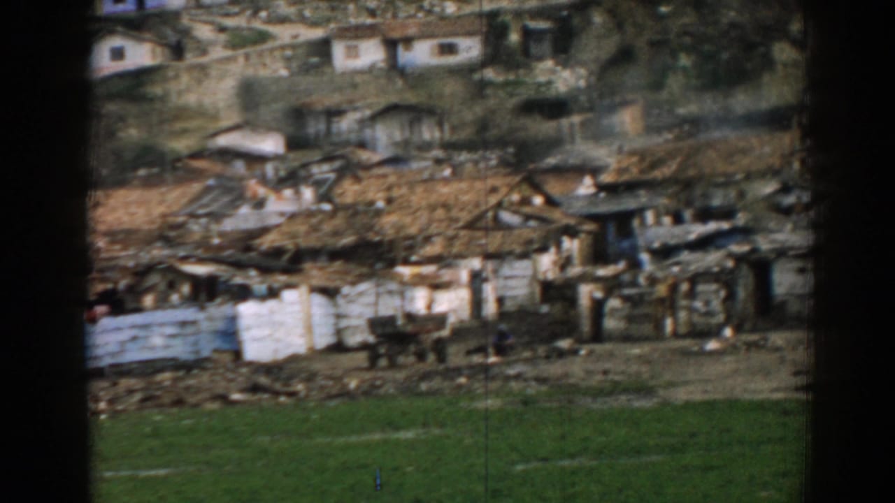 Weathered homes and fencing on a rocky hillside with grass in the foreground.