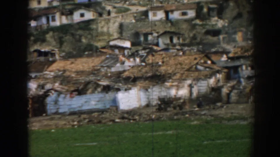 1962 Izmir home-movie view of clustered hillside homes, corrugated materials, uneven ground, and grass below.