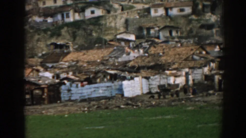 1962 Izmir frame showing modest hillside housing, patched fencing, rough ground, and a small cart near the grass.