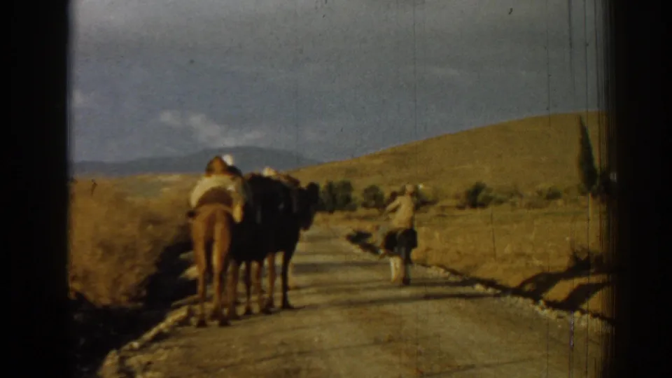 1962 8mm frame from Izmir, Turkey, showing a camel rider and another figure moving along a road through dry countryside.