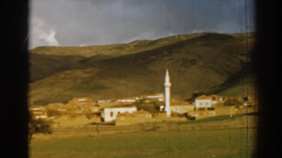 Wide 1962 Izmir-area village view with pale buildings, a white minaret, open fields, and low hills beyond.