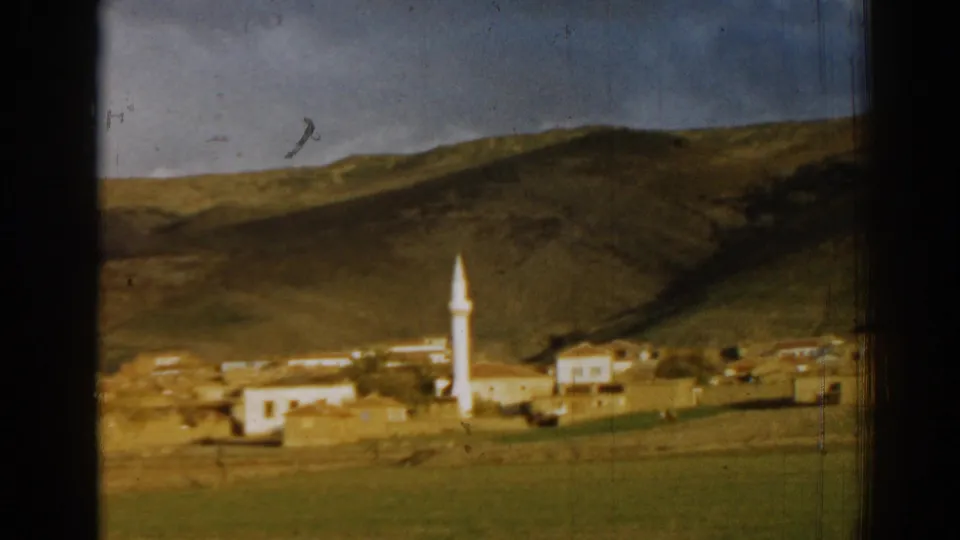 Vintage 1962 8mm frame near Izmir showing the village from a distance, with the minaret centered against hills and visible film wear.