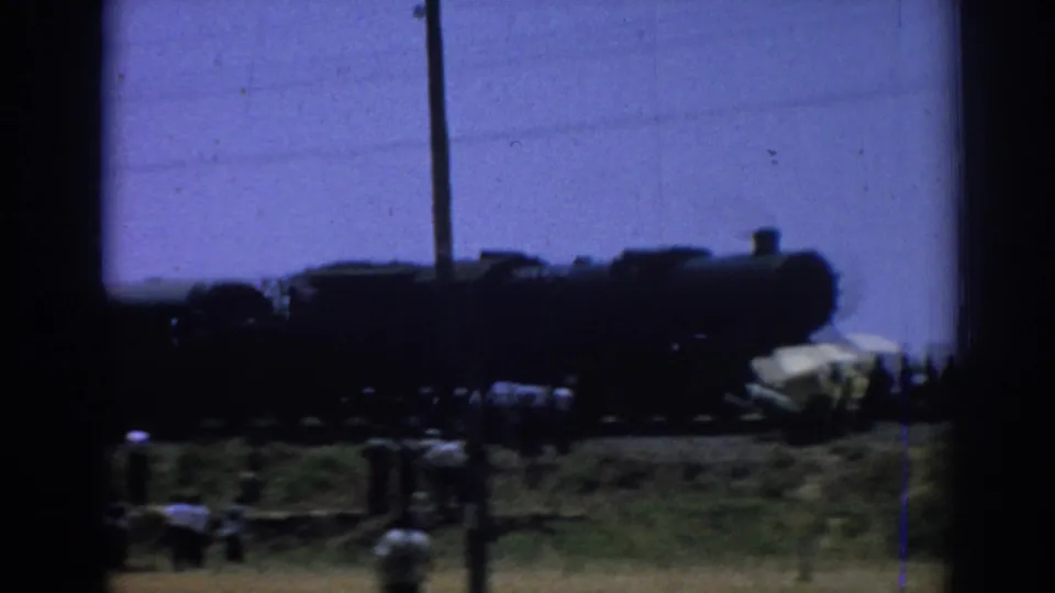 1962 Izmir frame of a stopped steam train partly blocked by foreground framing, with people standing along the rural rail line.
