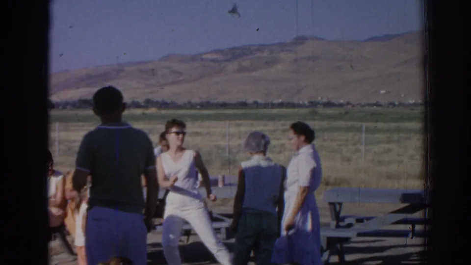 Several adults, including women in light dresses, gather around outdoor picnic tables in the Izmir-area 1962 home-movie scene.