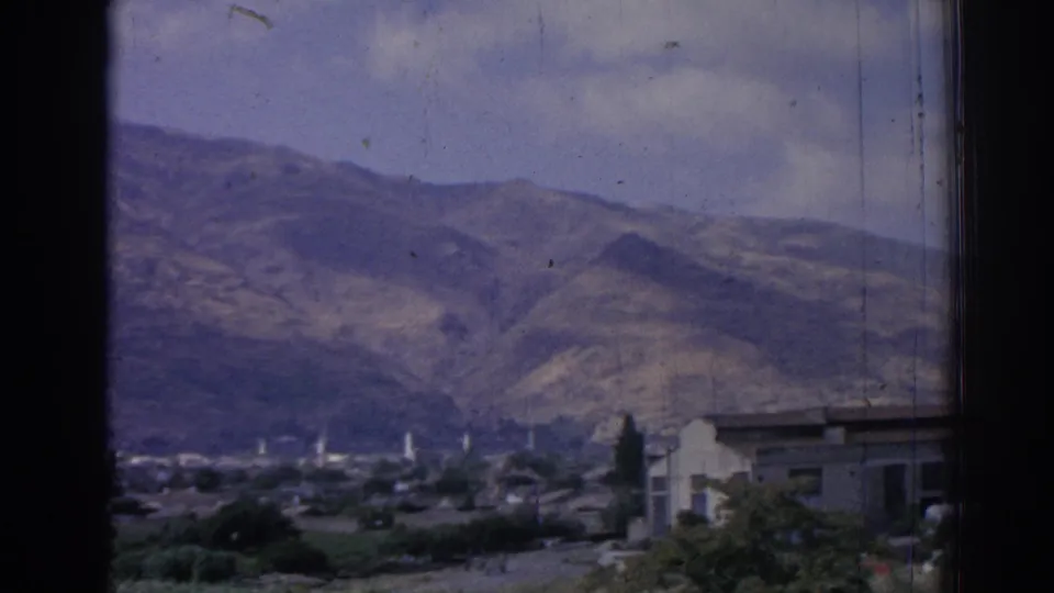 1962 Izmir hillside town view with a building edge in the foreground and rugged mountains beyond.