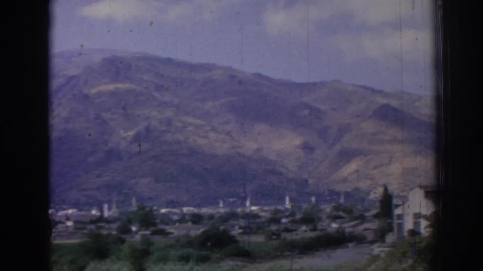 1962 Izmir home-movie frame showing a wide mountain backdrop above distant town structures and greenery.