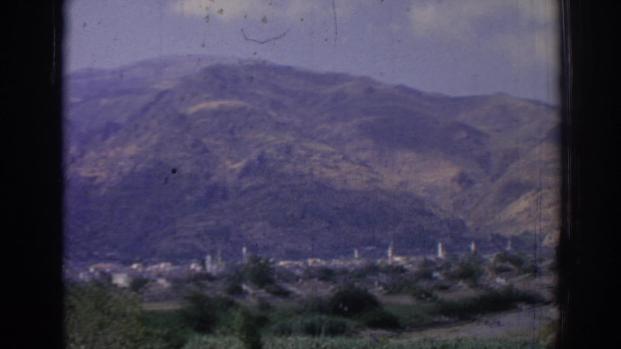 1962 8mm view of mountainous Izmir, Turkey, with a distant valley town, minarets, trees, and dark vertical foreground framing.