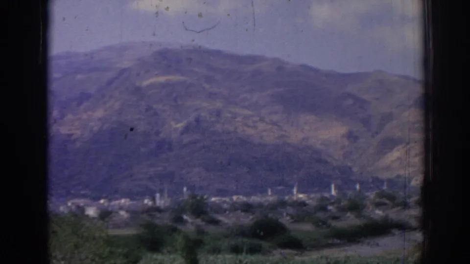 1962 8mm view of mountainous Izmir, Turkey, with a distant valley town, minarets, trees, and dark vertical foreground framing.