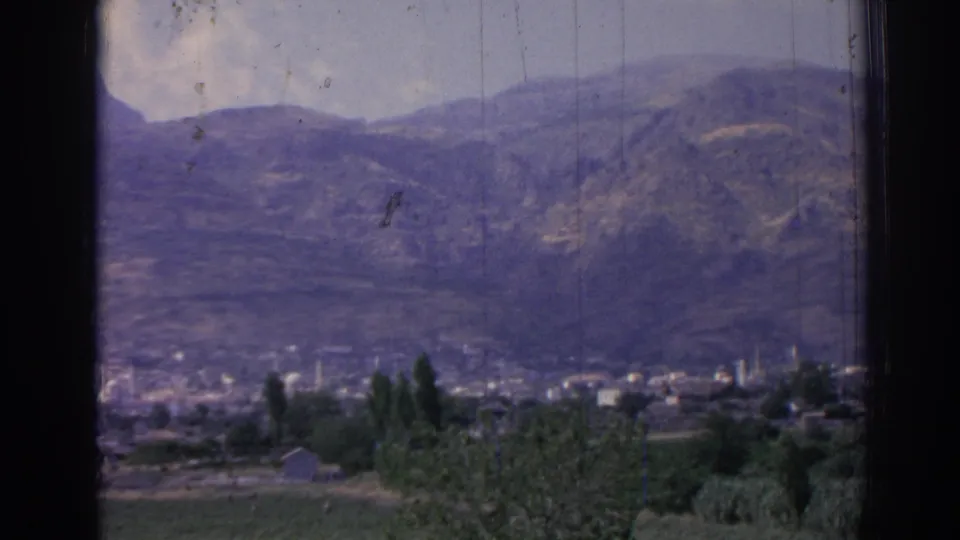 1962 8mm frame of Izmir, Turkey, showing a valley settlement with minarets, trees, fields, and mountain slopes in the background.