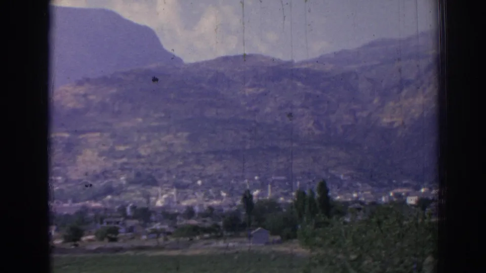 1962 8mm view of mountainous Izmir, Turkey, with a distant town, visible minaret, trees, open fields, and a small pale foreground structure.