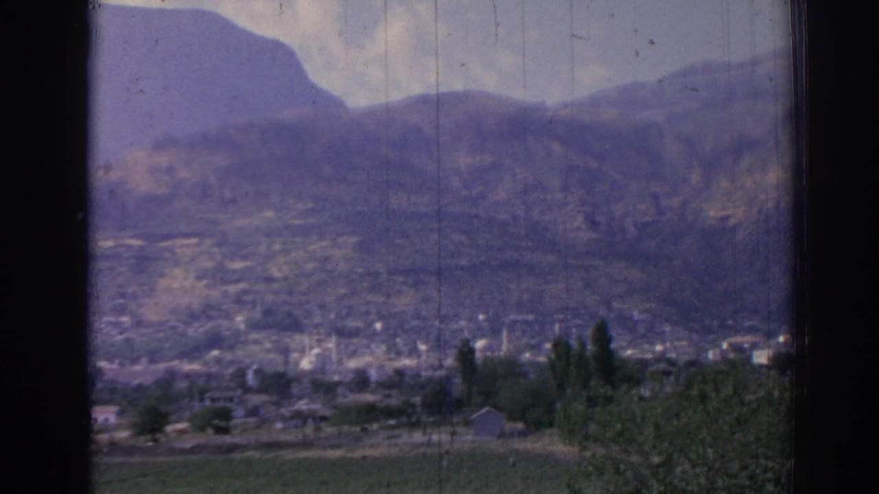 Town buildings and minarets below a mountain, seen through dark window edges.