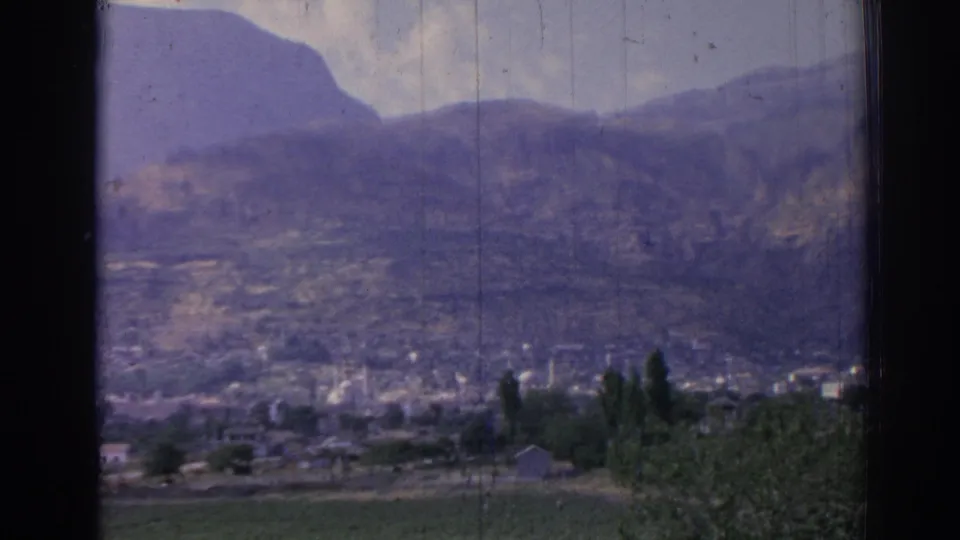 1962 Izmir home-movie view of distant buildings and minarets at the base of a rugged mountain, framed by dark window edges.