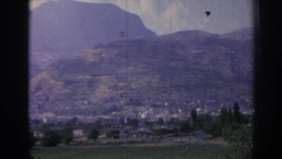 Soft 8mm frame of Izmir in 1962, showing a distant townscape with minarets, trees, and mountains beyond.
