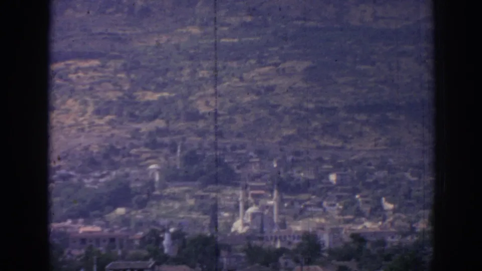 1962 8mm view over Izmir, Turkey, showing a distant city, mosque minarets, hills, and soft film grain from an elevated vantage point.