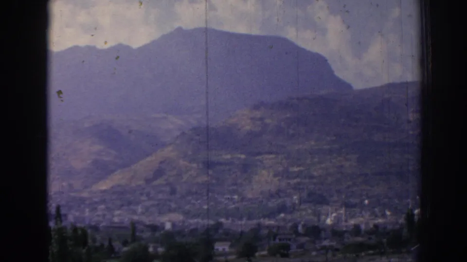 1962 Izmir home-movie frame with a mountain ridge, layered hills, distant urban area, and visible 8mm film wear.