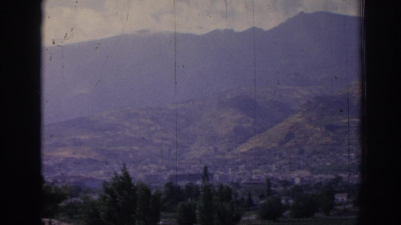 1962 8mm view from a window toward a hazy mountain valley in Izmir, Turkey, with foreground trees and distant settlement.
