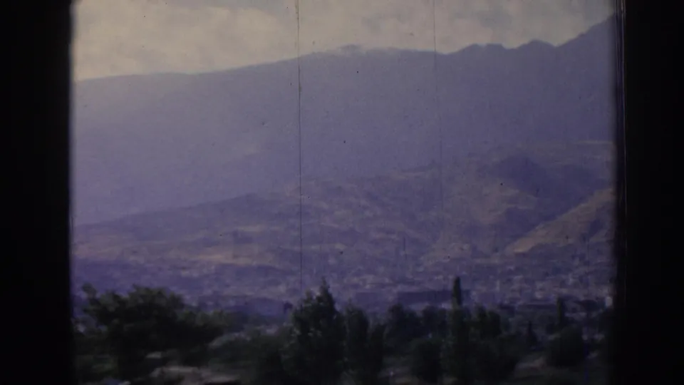 Window-framed 1962 Izmir landscape showing a broad valley below hazy mountains and a cloudy sky.